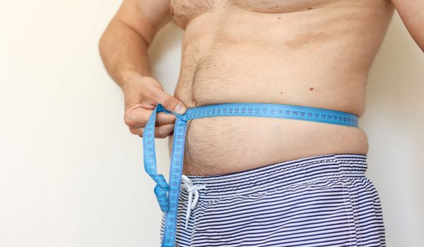 A man measures his fat belly with measuring tape. Concept of weight loss, health problems of obese people. Poor nutrition and sedentary lifestyle. Increased risk of heart illnesses. World Obesity Day.