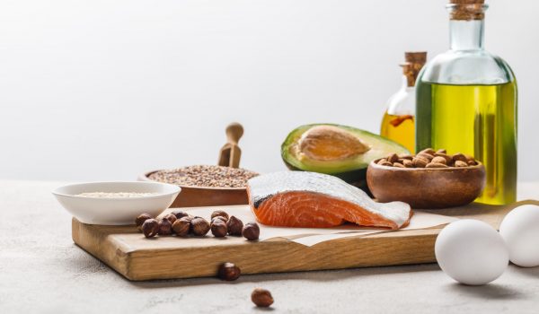 fresh raw salmon, nuts, eggs and avocado on wooden chopping board near oil isolated on grey,