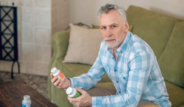 Calm attractive mature male with plastic bottles in his hands sitting on the sofa in a room