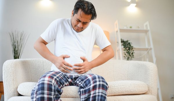 Sad exhausted guy of indian and arabian ethnicity, holds his hands on his stomach, grimaces from pain in his stomach, suffers from poisoning, spasm, stomach problems.