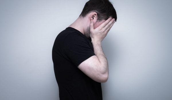 An upset guy in a black sweater hiding his face with hands