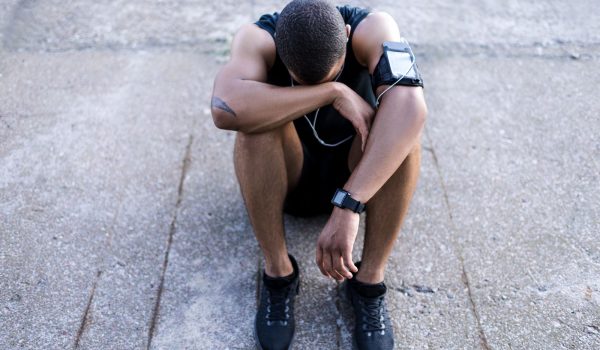 young african american sportsman listening music in earphones while sitting on pavement